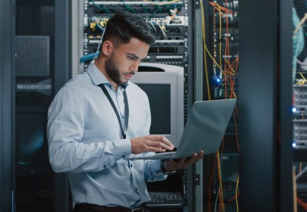 Server expert working on laptop in front of servers. Server expert working on laptop in front of servers.